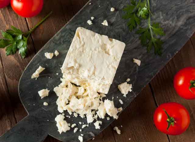 A mold of homemade cheese on a wooden cedar board and a few sprigs of parsley and tomatoes next to it