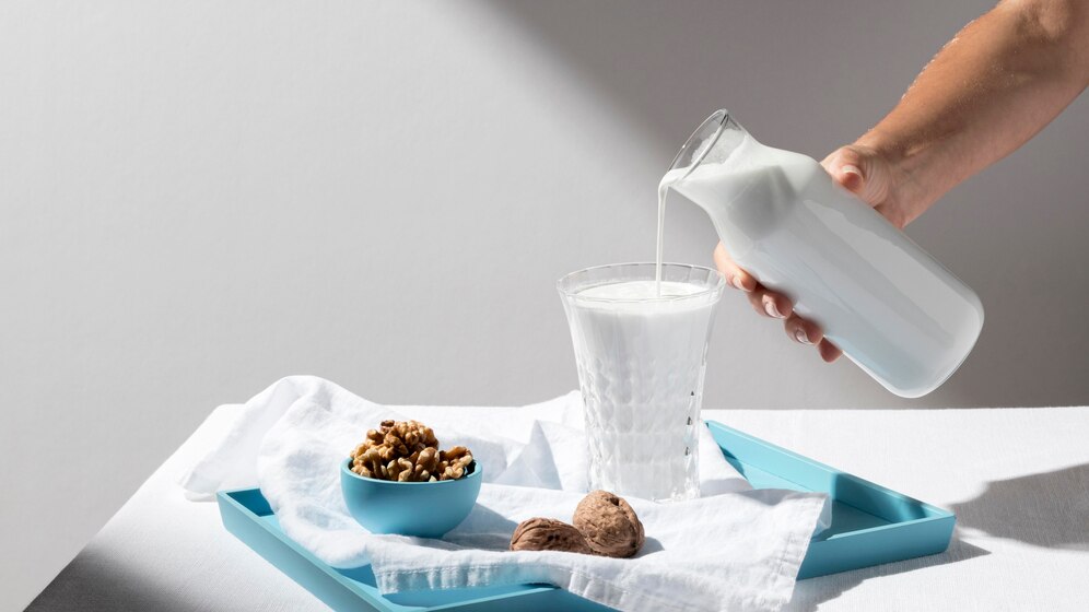 person-pouring-milk-full-glass-with-walnuts-tray