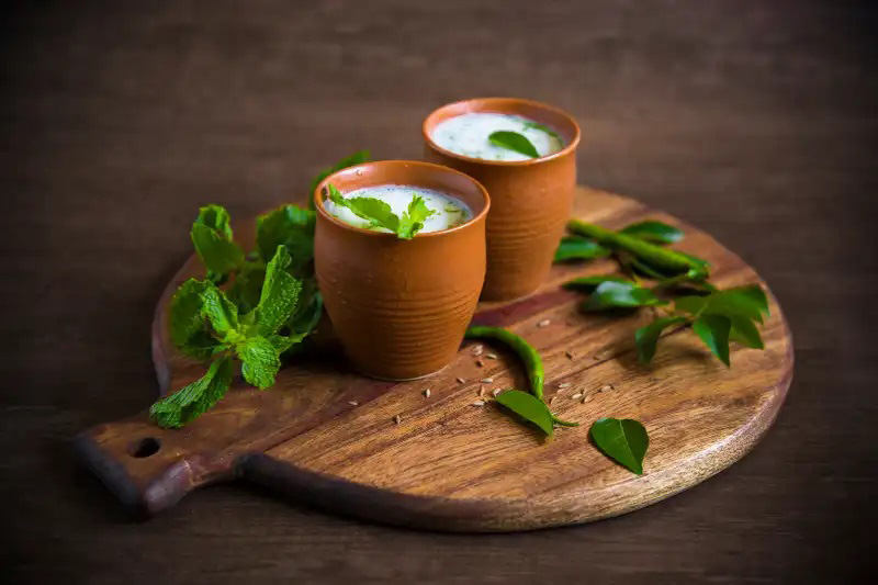 Two glasses of buttermilk in clay glasses on a wooden cedar board with mint leaves next to it