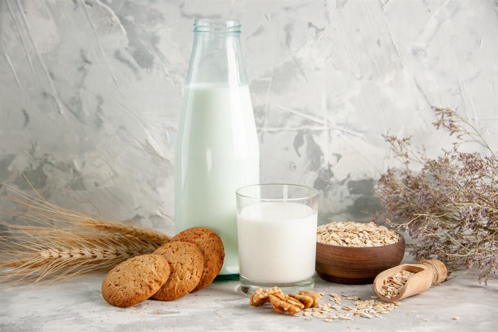 top-view-glass-bottle-cup-filled-with-milk-wooden-tray-cookies-spoon-oats-brown-pot-spike-white-table-ice-background